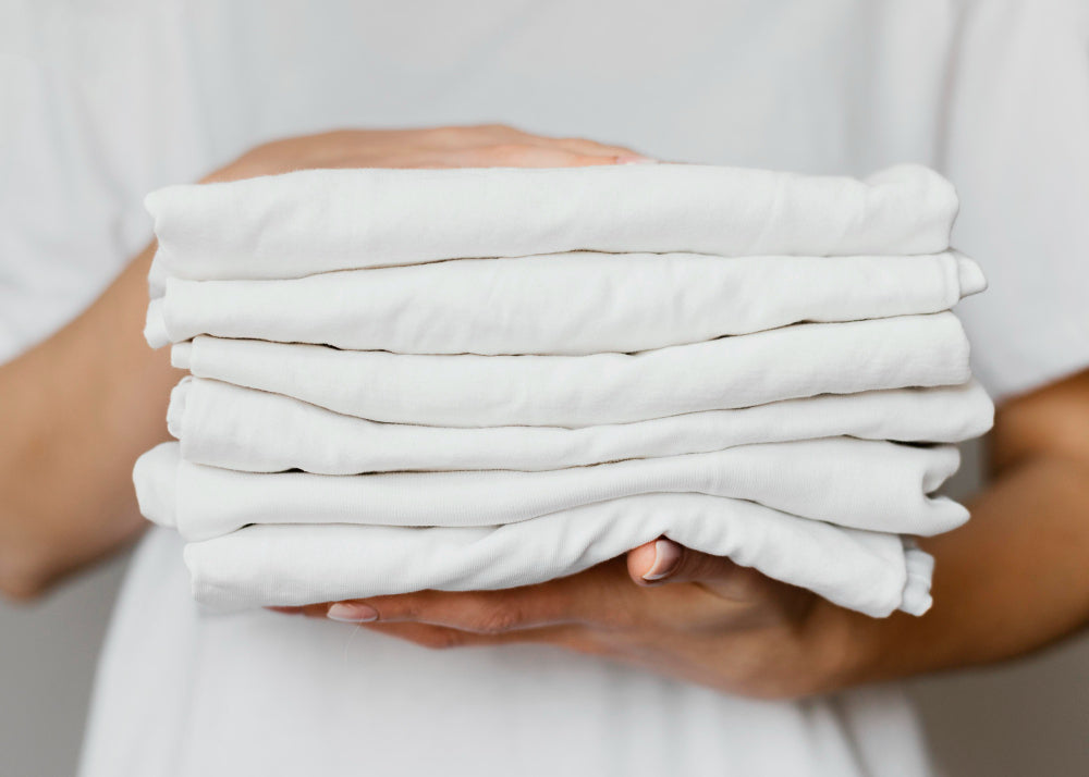 A person holding a neatly folded stack of clean white bed sheets, symbolizing fresh bedding and good sleep hygiene.
