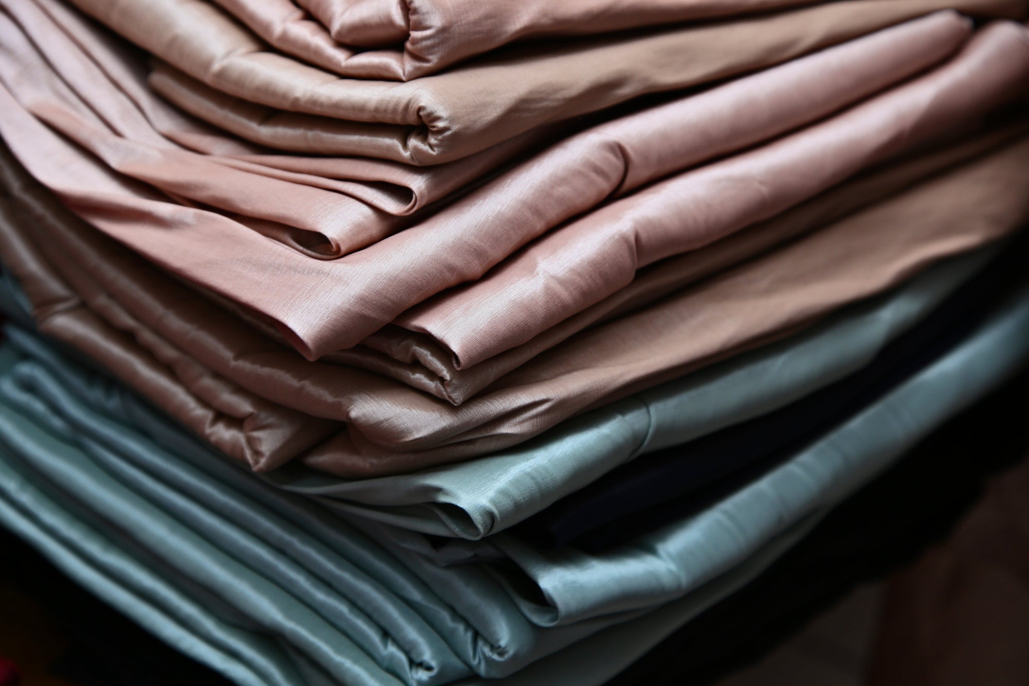 Stack of folded pastel-colored fabrics showcasing the smooth, breathable texture of the best TENCEL sheets for luxury and comfort.