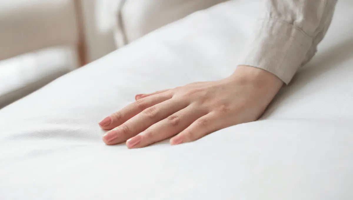 Hand resting on breathable light gray cooling bed sheet fabric.
