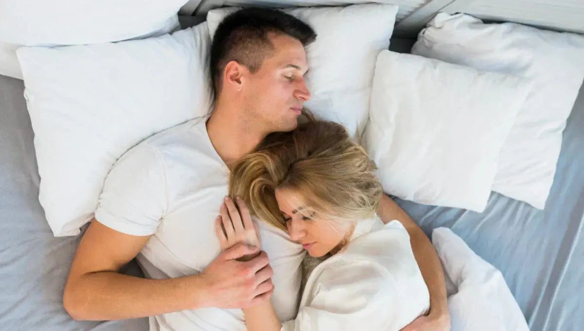 Couple sleeping face to face in a loose cuddle, with one partner resting their head on the other’s chest.
