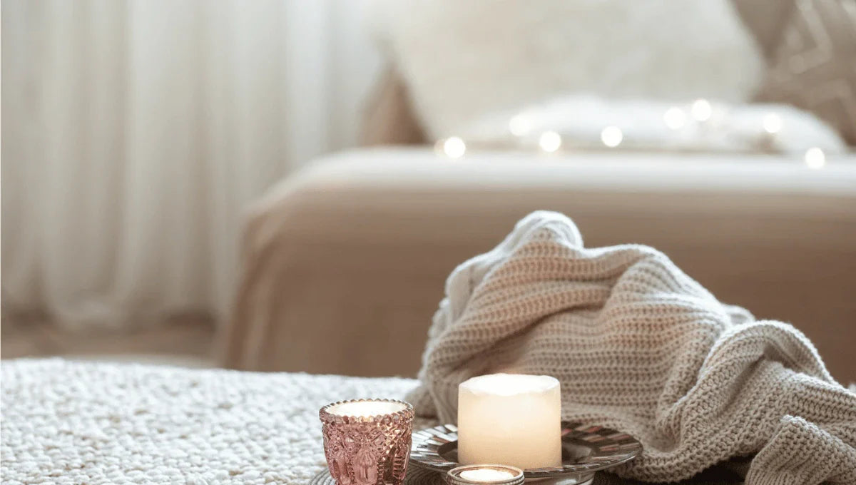 Cozy bedroom scene with candles, soft knit blanket, and warm textures for staying comfortable during winter.