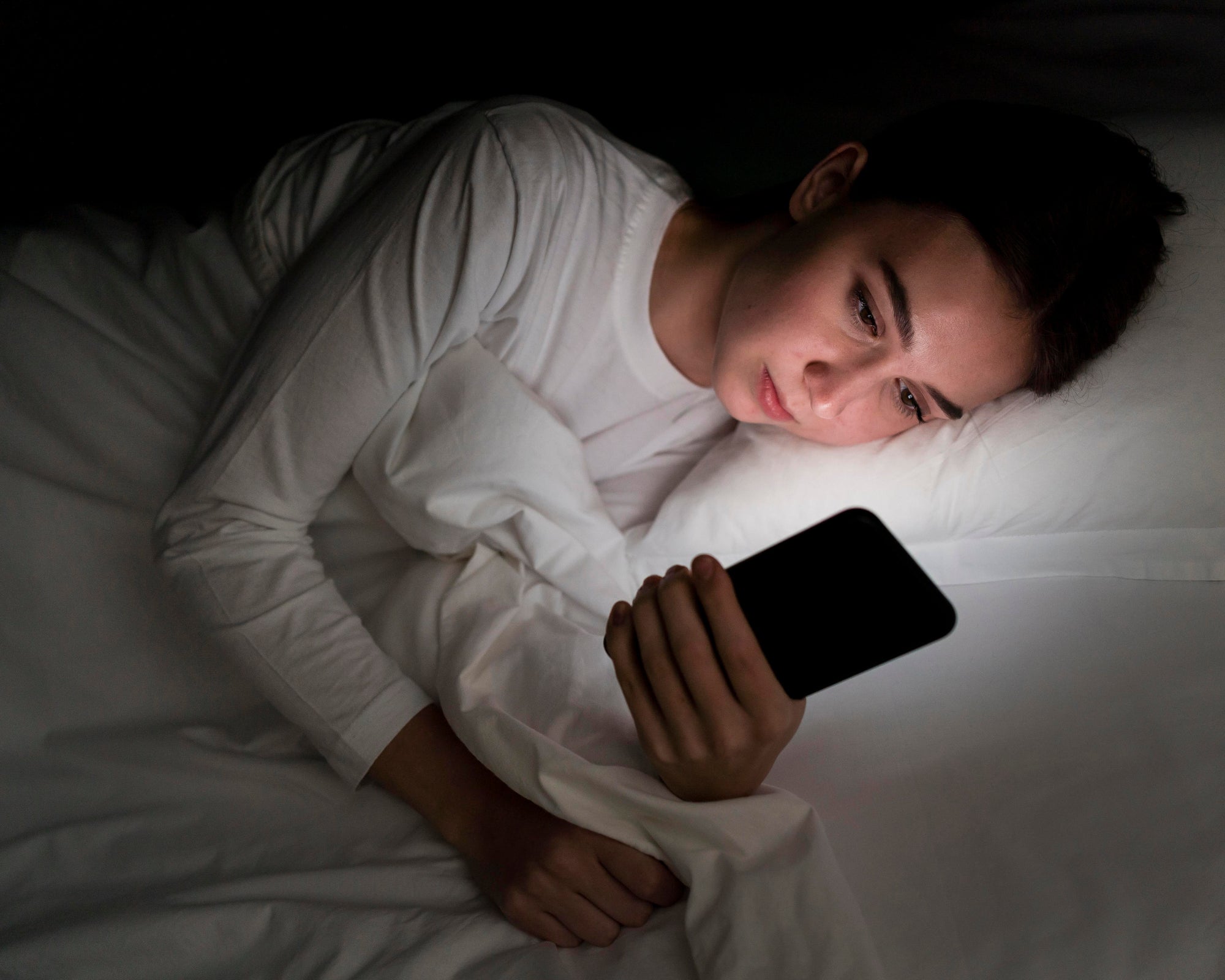 Woman struggling to fall asleep at night because of phone use, highlighting the need for digital detox tips.