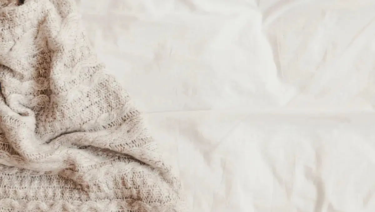 Textured knit blanket resting on soft white bed sheets, showing how friction from rough fabrics can contribute to sheet pilling.