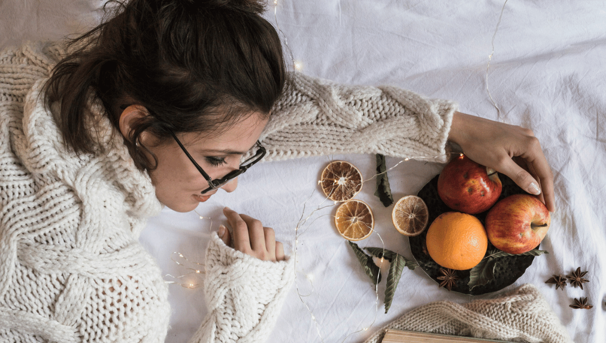 Woman relaxing in a cozy sweater with seasonal fruit and soft lighting, representing Thanksgiving wellness and rest.