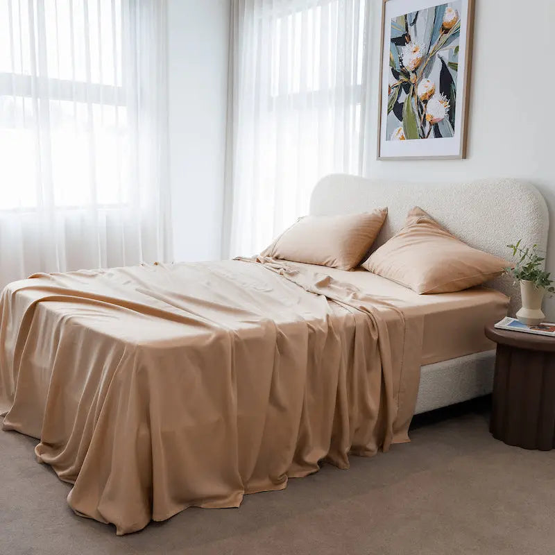 Neatly made bed with beige bedding in a bright bedroom.