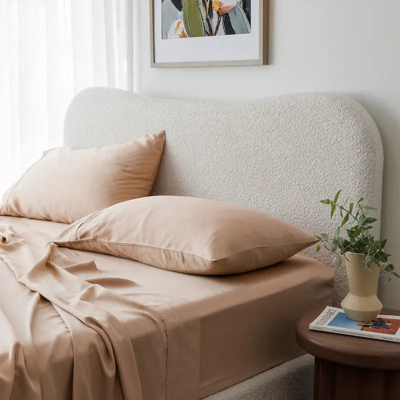 Neatly made bed with beige pillows and bedding in a well-lit bedroom.