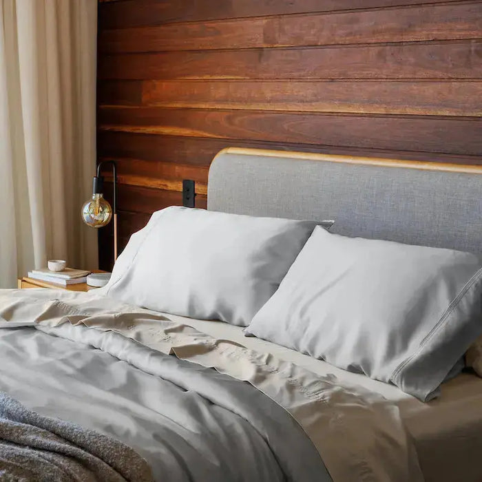 Bedroom with a bed featuring gray bedding and pillows against a wooden wall. #color_gray mist