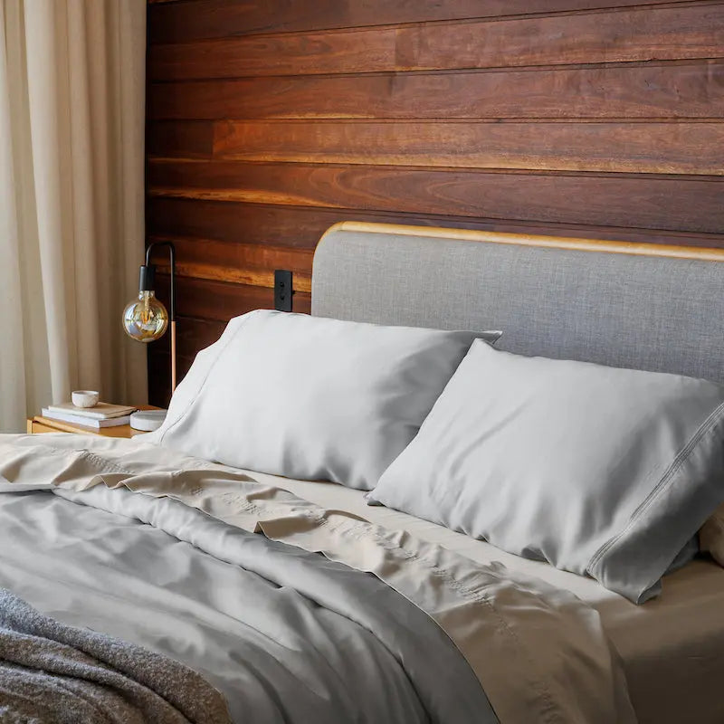 Bedroom with a bed featuring gray bedding and pillows against a wooden wall.