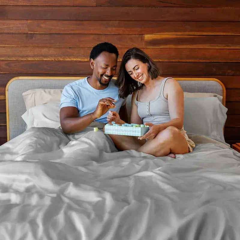 Man and woman sitting on a bed, looking at a box together in a bedroom setting.