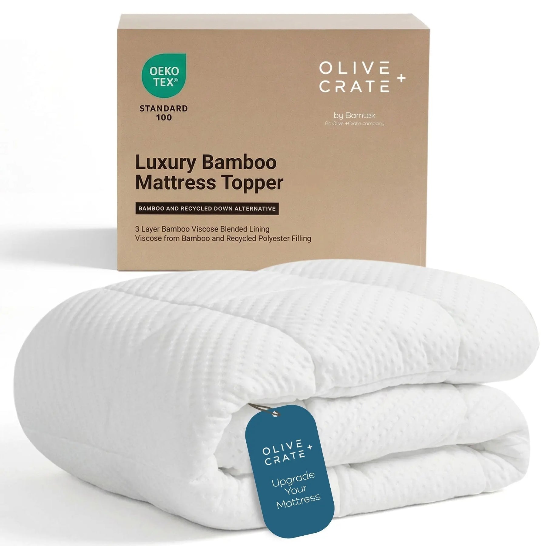 A folded white bamboo mattress topper with a blue hangtag sits in front of its kraft paper packaging box. The box is branded 'Olive Crate' and features a green 'DEKO TEX Standard 100' label.