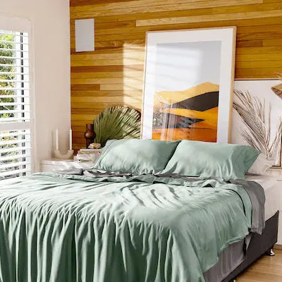 Neatly made bed with green bedding in a bedroom with wooden wall and decor.