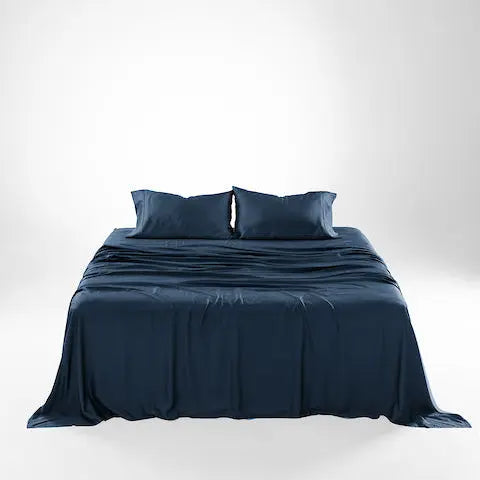 A neatly made bed with dark navy blue bedding, including a duvet cover and two matching pillows, photographed against a clean white studio background. French Navy sheet set