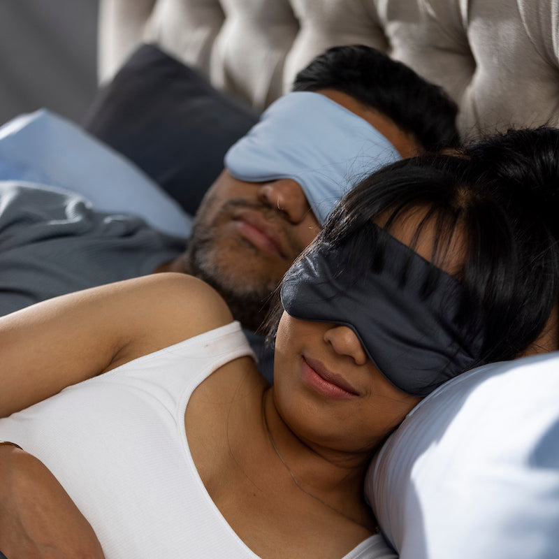 Two people lying down with eye masks on, possibly in a bedroom setting.