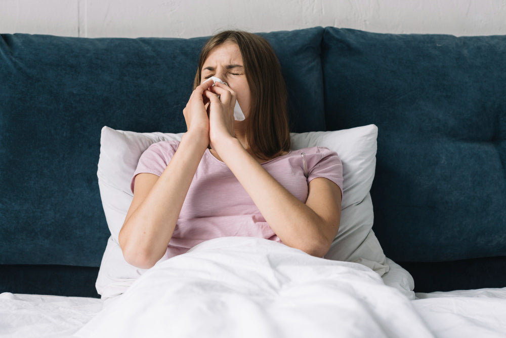 Woman in bed sneezing due to nighttime allergies, holding a tissue while trying to rest.