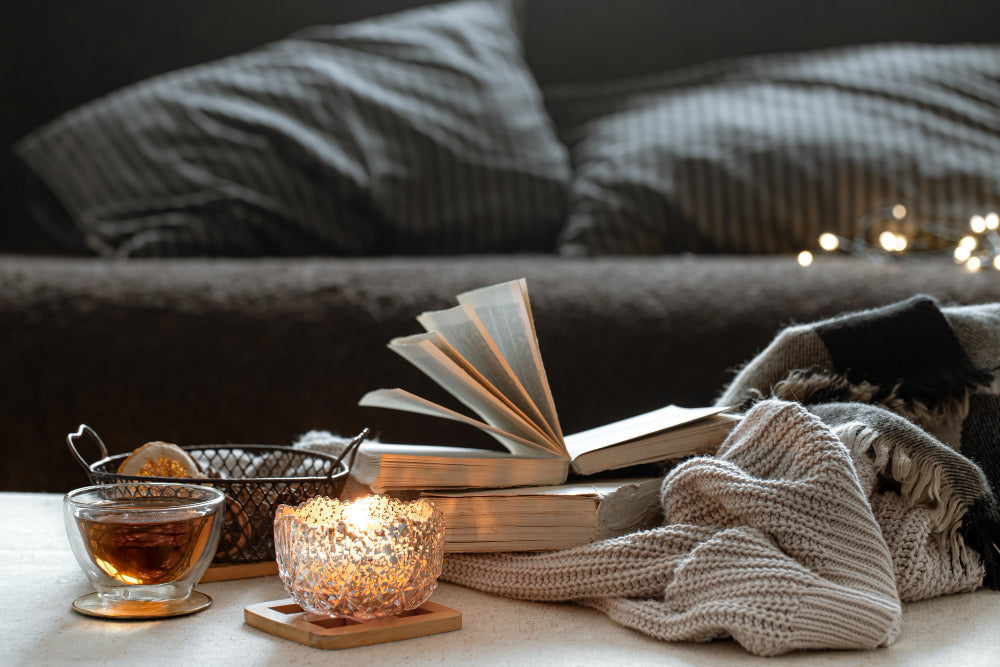 A cozy fall setup with a lit candle, a cup of tea, and an open book surrounded by soft blankets, creating a warm and relaxing evening atmosphere.