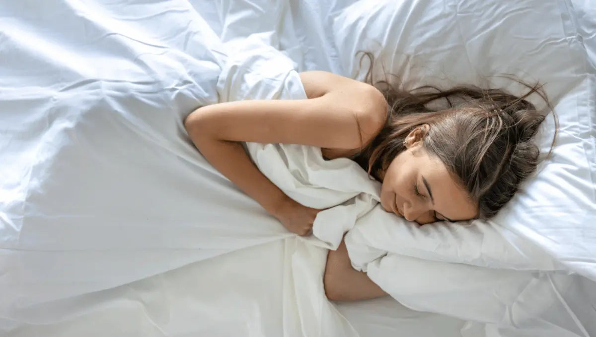 Woman sleeping comfortably in white bedding, illustrating cooler and more comfortable sleep without heavy sleepwear.