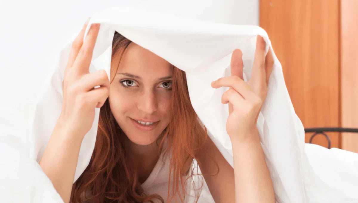 Woman lying under white bed sheets, highlighting smooth breathable bedding for sensitive skin.