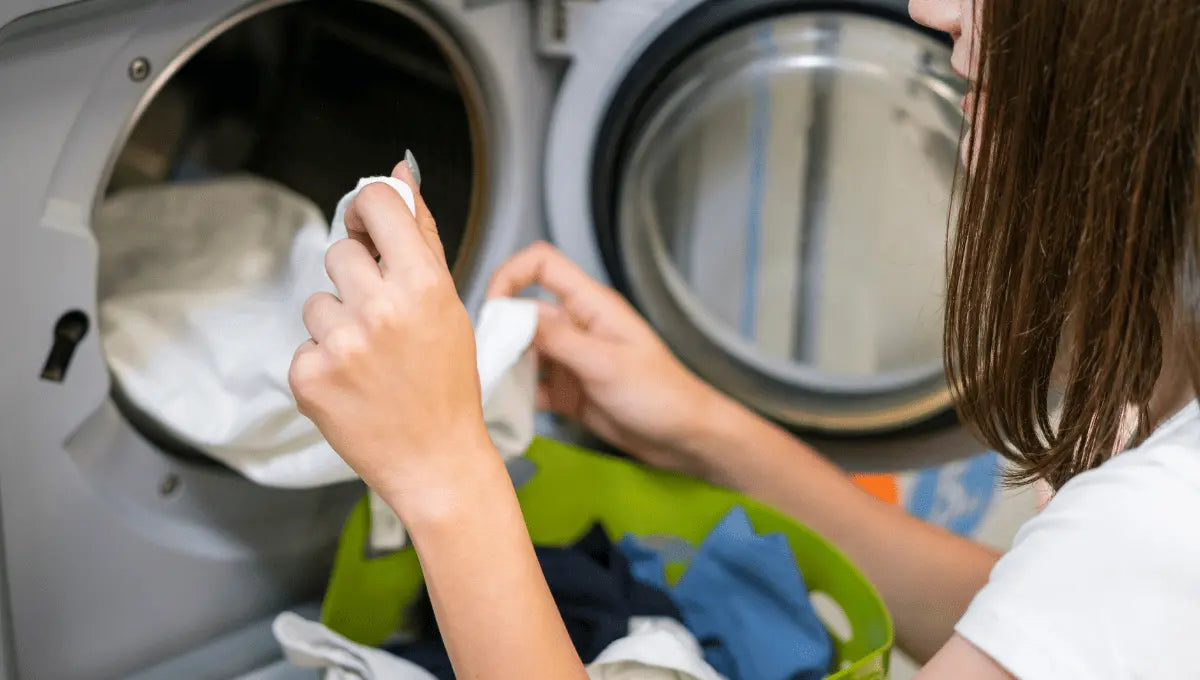 Hands gently placing sheets into a washing machine, showing proper care for delicate bedding fabrics like TENCEL.