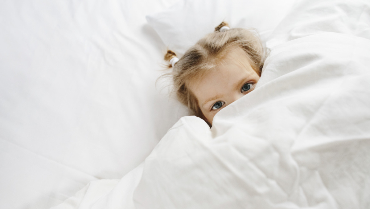 Child resting under white bedding, illustrating skin-safe sheets and OEKO-TEX certified fabric for sensitive sleepers.