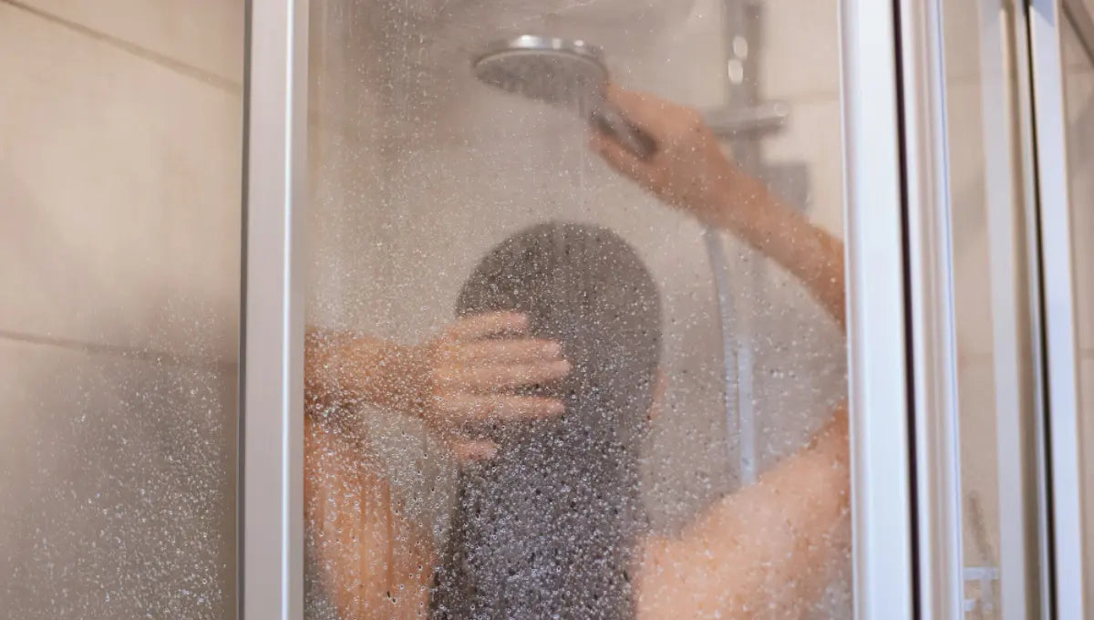 Person taking a shower behind a glass door, illustrating a cold shower before bed routine.
