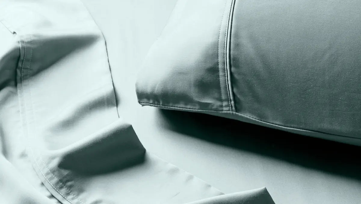 Close-up of soft sage green eucalyptus TENCEL™ bed sheets and pillowcase with smooth, breathable fabric texture.
