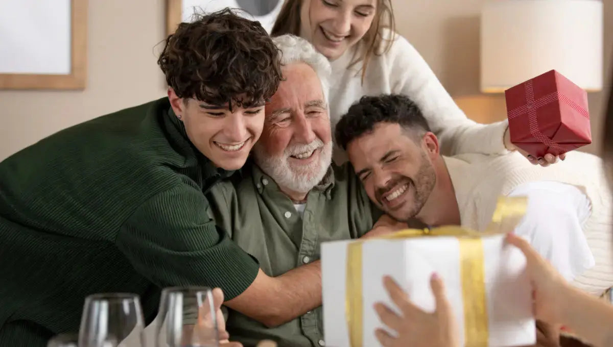 Family gathered around an older father smiling while receiving gifts at home on Father's Day.