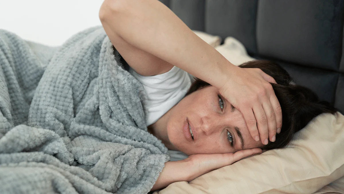 Person lying awake in bed under blankets, appearing uncomfortable and overheated during sleep.