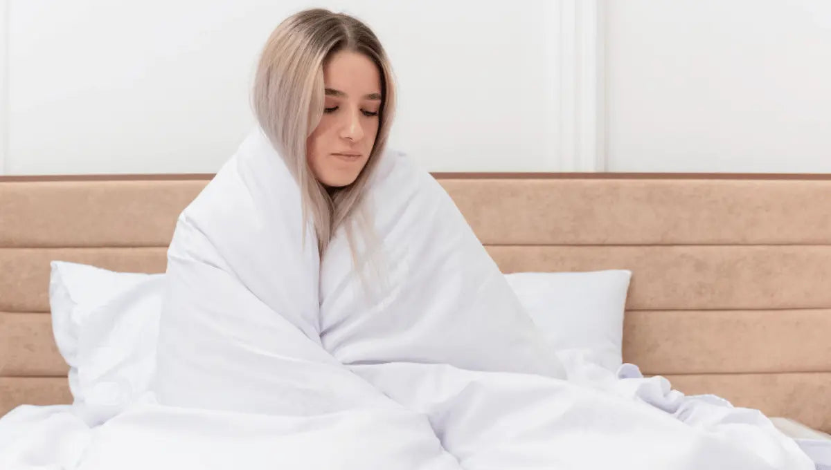 Woman wrapped in a breathable white comforter, sitting comfortably on a bed.