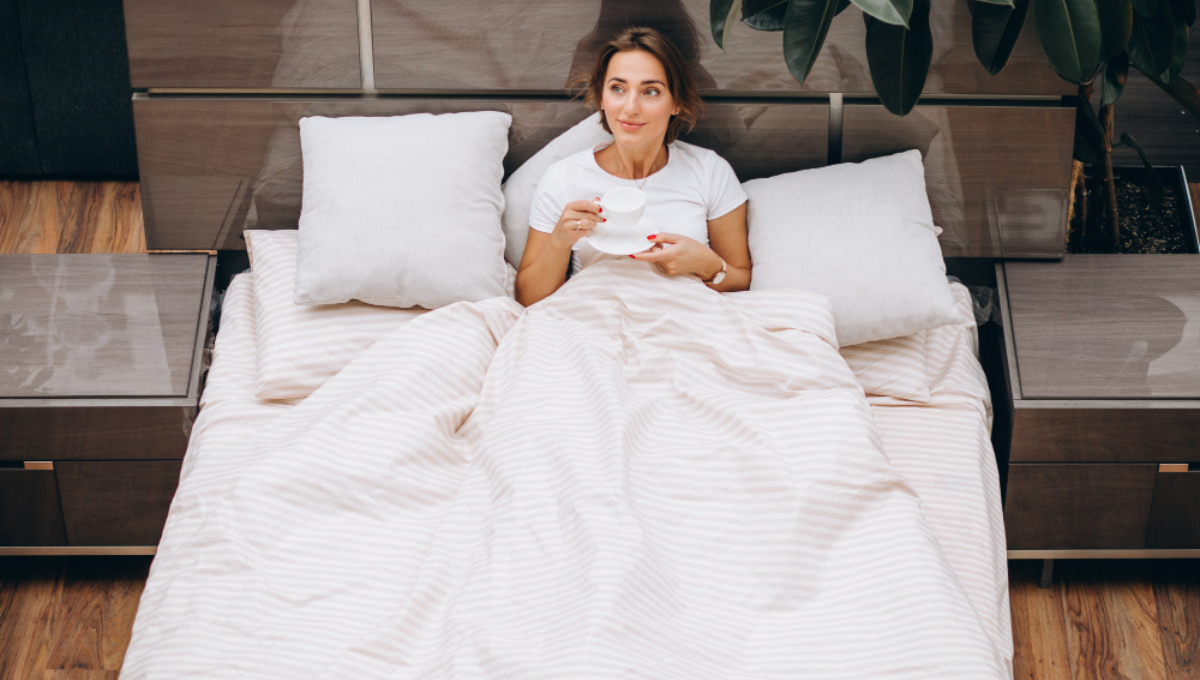 Woman sitting in bed with striped bedding while comparing sheet materials for comfort and sleep temperature.