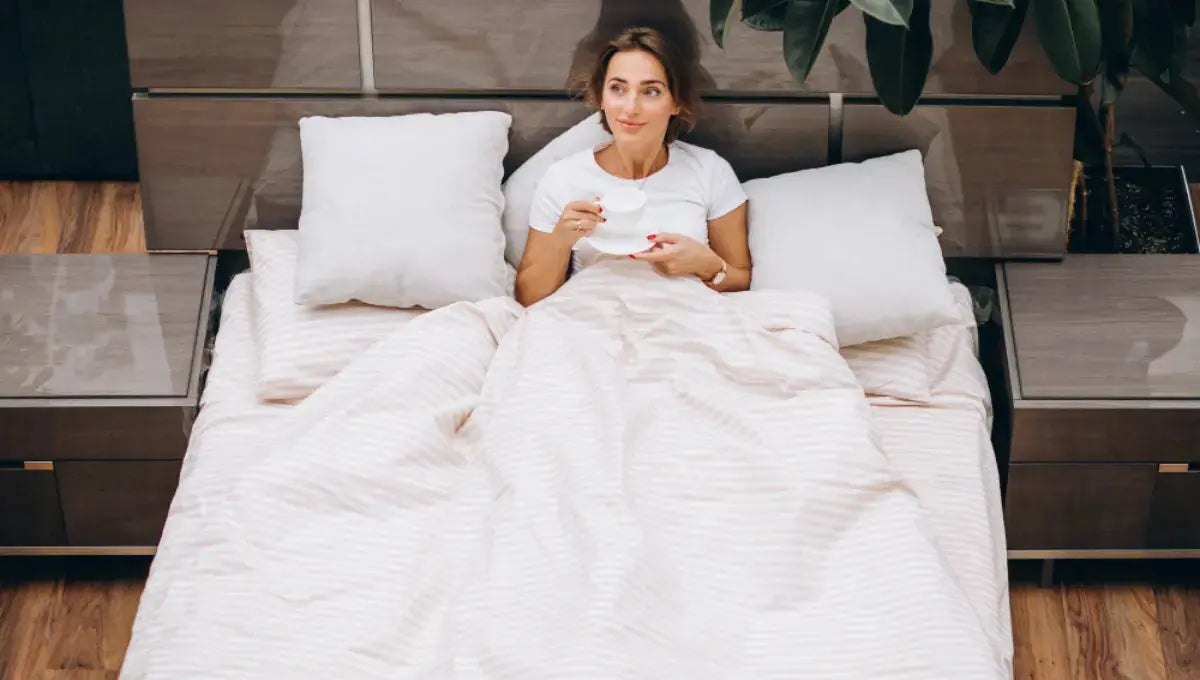 Woman sitting in bed with striped bedding while comparing sheet materials for comfort and sleep temperature.