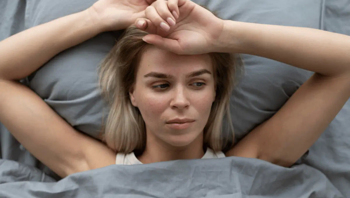 Woman lying awake in bed under gray bedding, illustrating how bedroom temperature can affect sleep comfort.