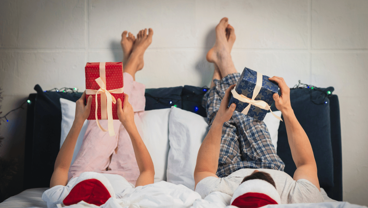 Couple relaxing in bed holding wrapped Christmas gifts, creating a cozy and comfortable holiday moment.