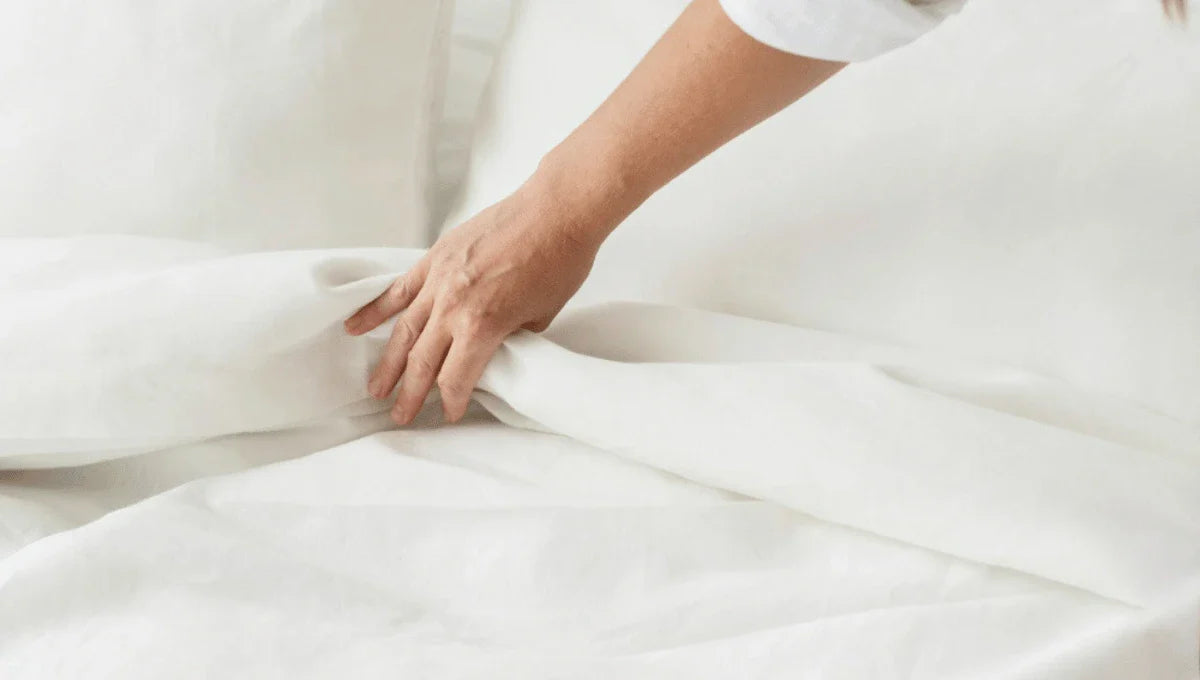 Person smoothing a white duvet on a neatly made bed.