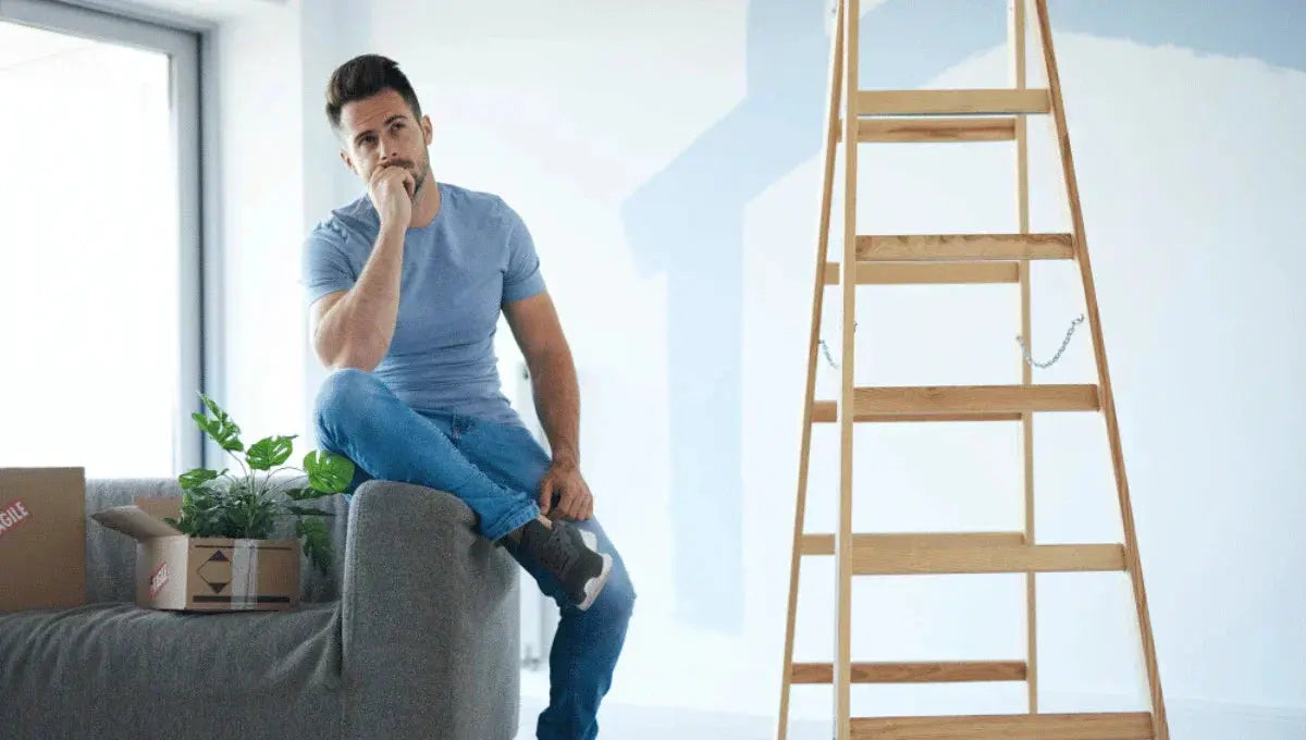 Man sitting on a couch in a partially painted living room, planning home upgrades before selling.