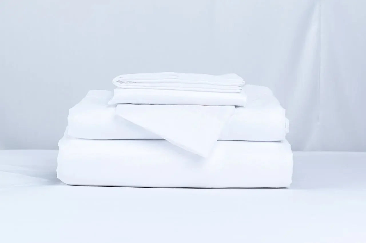 Neatly folded white fitted sheet and bedding stacked on a bed.