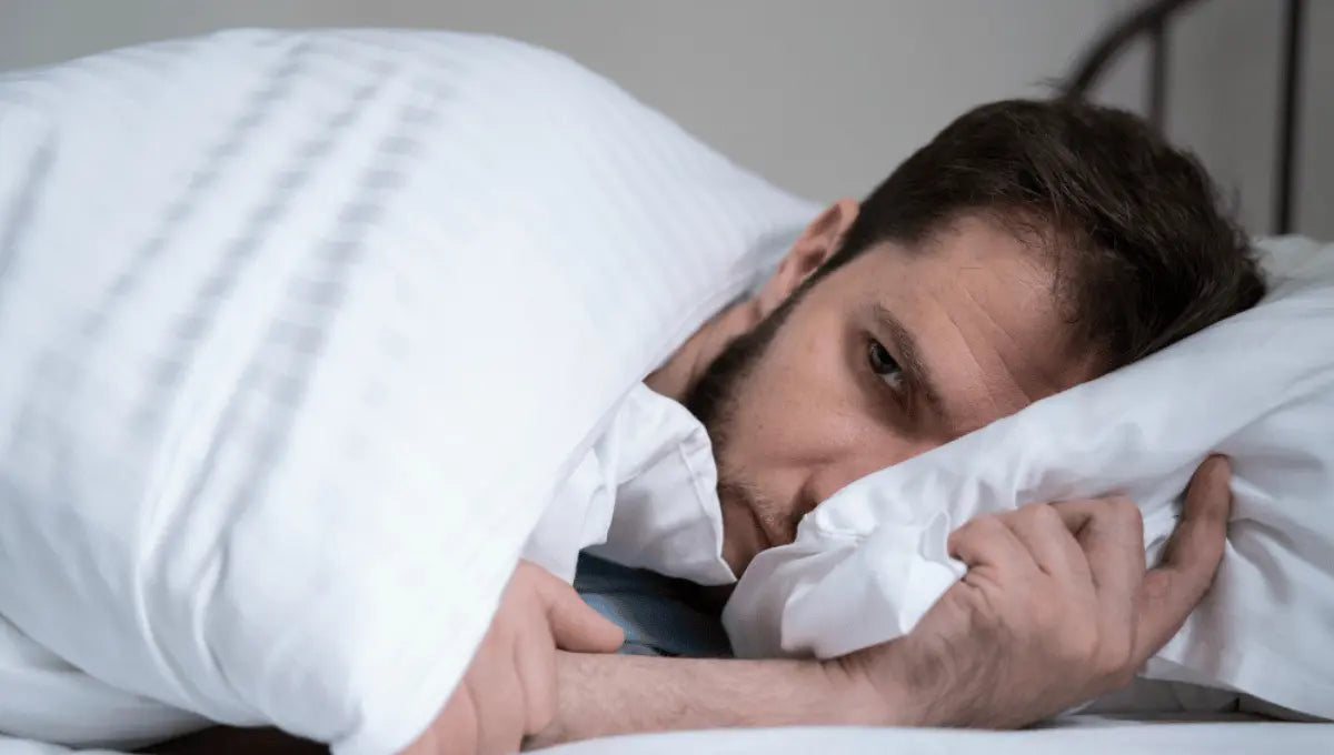 Man lying awake in bed under blanket appearing uncomfortable from nighttime overheating or night sweats.