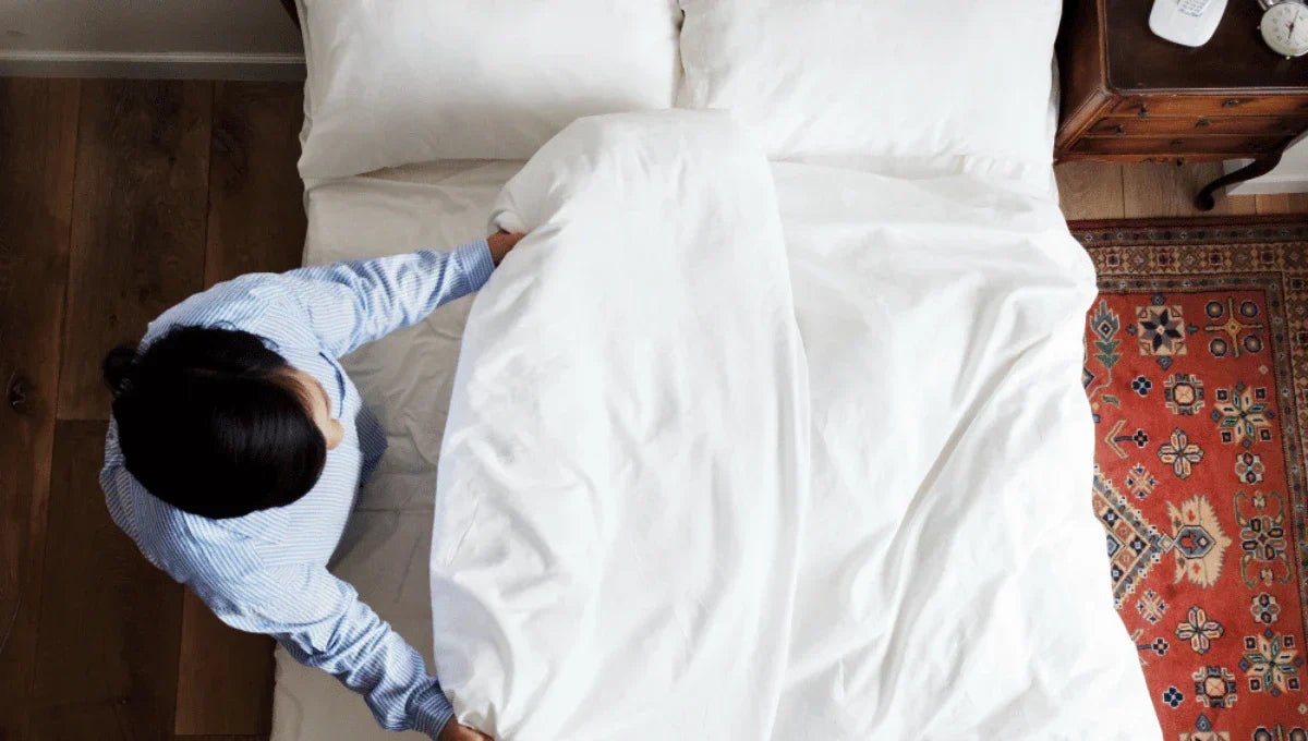 Person adjusting a white duvet cover on a neatly made bed viewed from above.