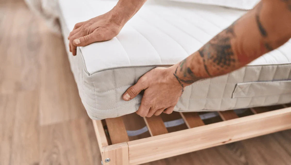 Person positioning a mattress on a wooden bed frame during setup.