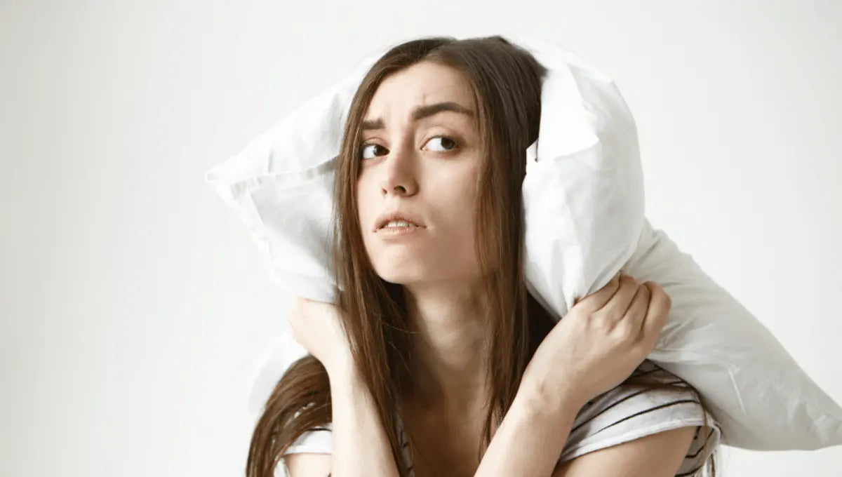 Woman holding pillow over her ears while awake in bed, illustrating common sleep myths and nighttime restlessness.