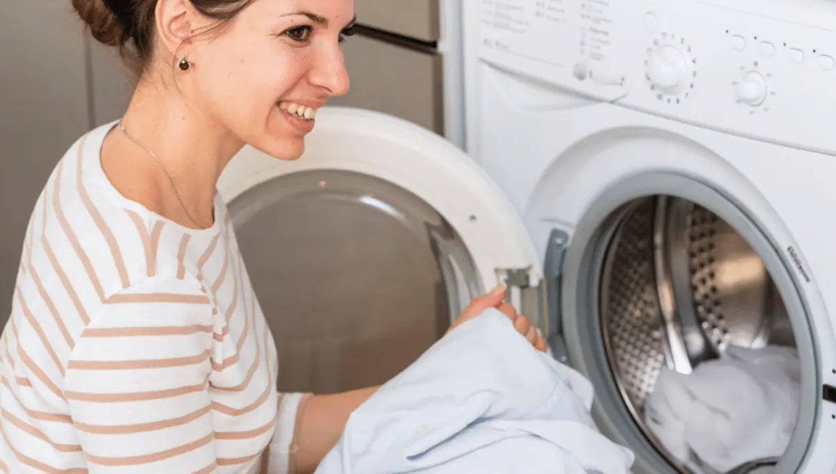 Person placing white bed sheets into a washing machine for laundry.
