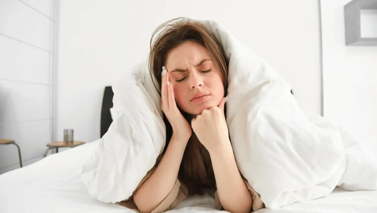 Person lying in bed with pillows, looking uncomfortable and restless while trying to sleep.