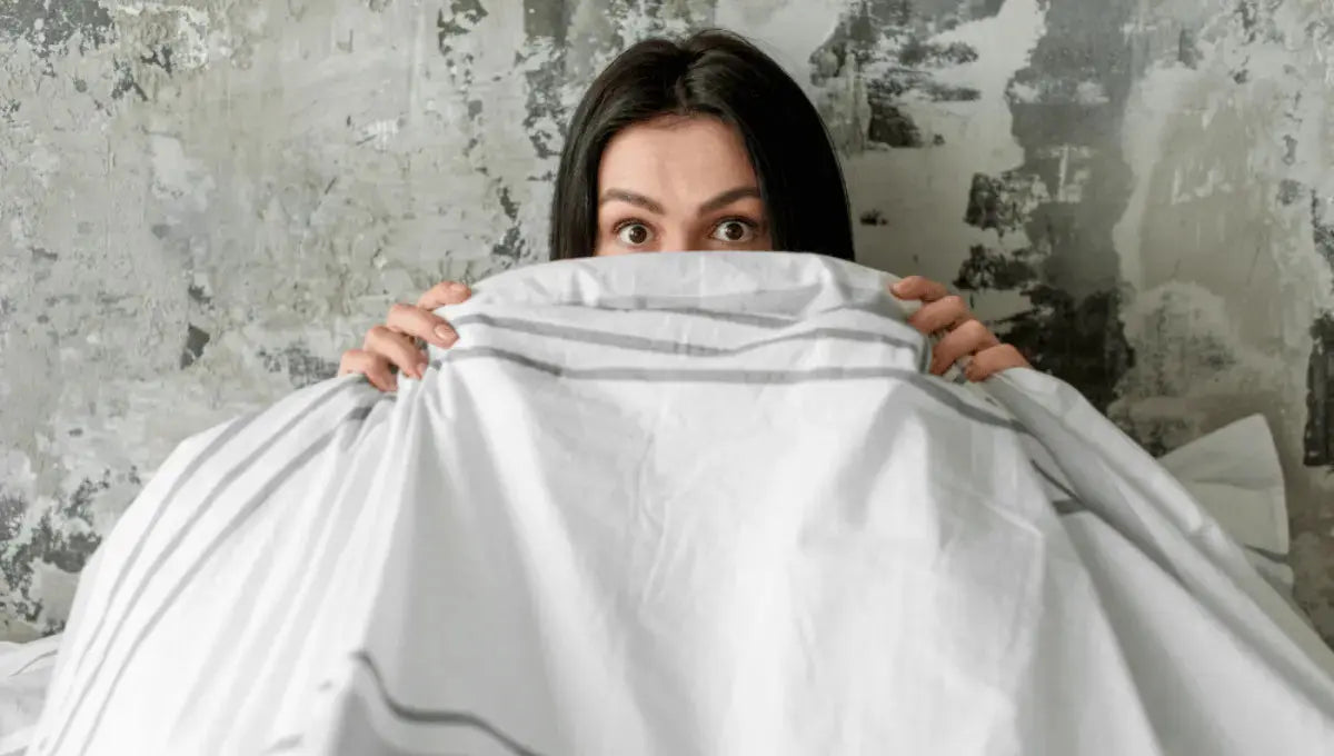 Woman partially covered by bed sheets, reacting to feeling too warm under synthetic bedding.