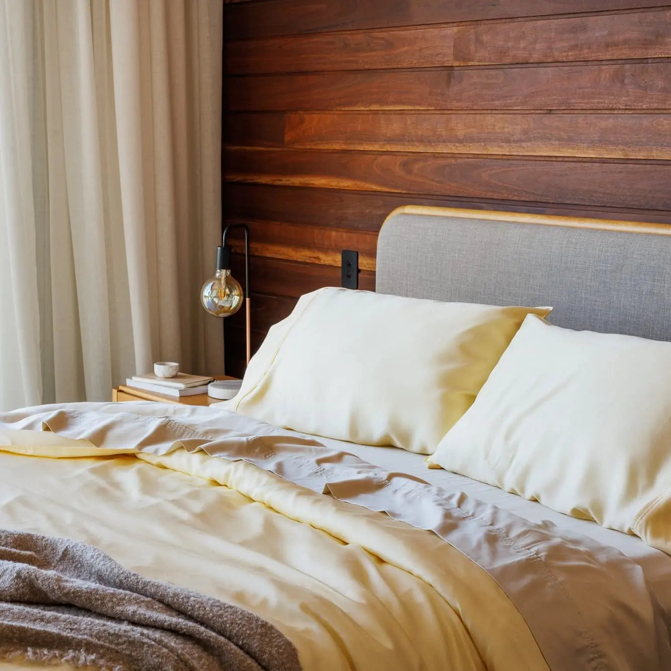 Bedroom with wooden wall, bed with white bedding, and lamp. 