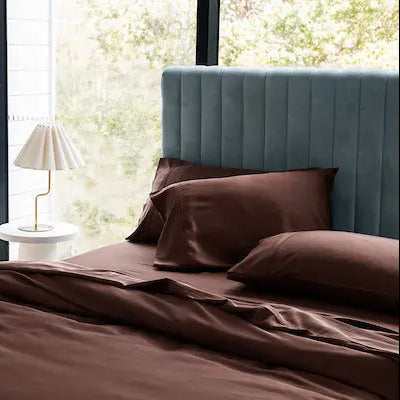 Bedroom with brown bedding, teal headboard, and a plant on a windowsill. 