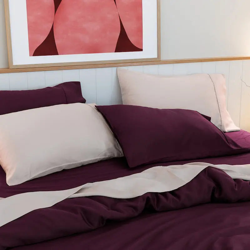 Bed with sour cherry and dusk bedding, framed artwork on the wall.  