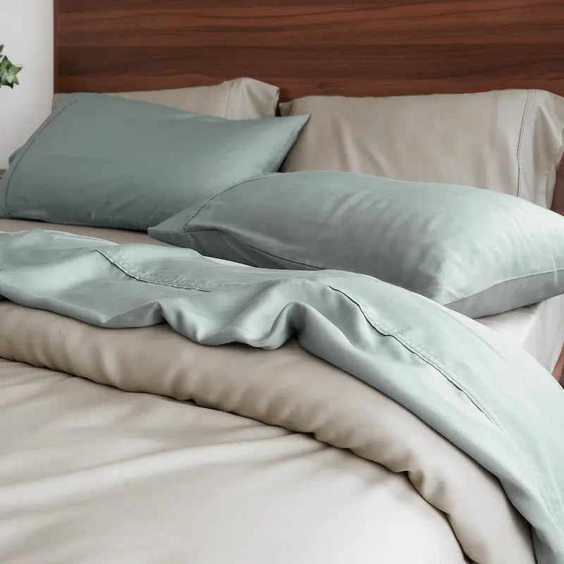 Bed with light green bedding and pillows in a bedroom setting. 