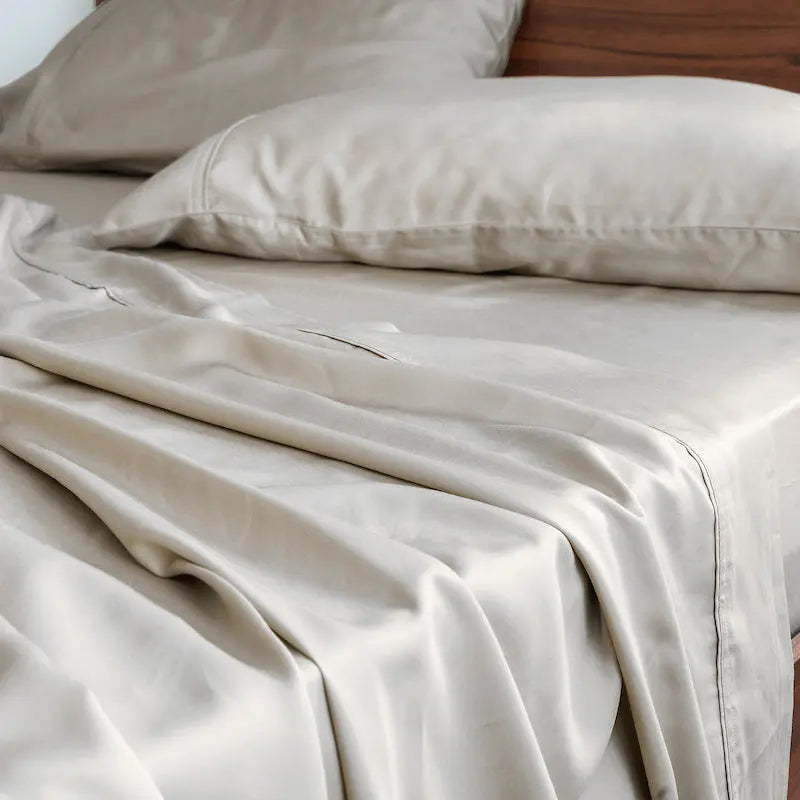 Beige bedding set on a bed with wooden headboard. 