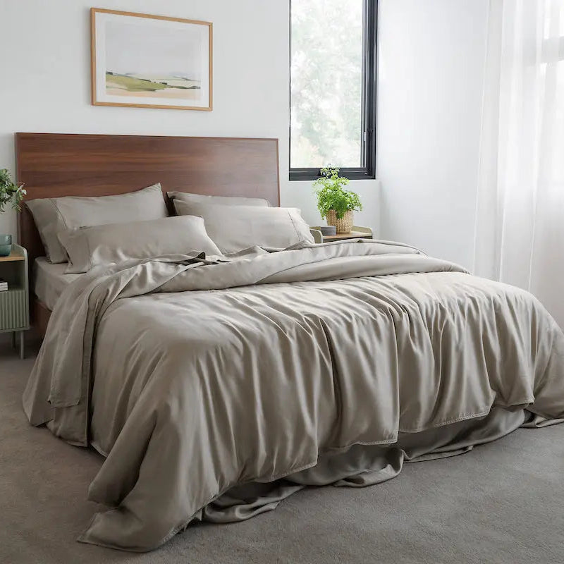 Neatly made bed with beige bedding in a bright bedroom. 