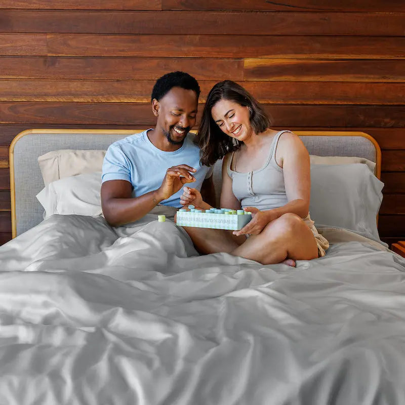 Man and woman sitting on a bed, looking at a box together in a bedroom setting. 