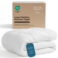 A folded white bamboo mattress topper with a blue hangtag sits in front of its kraft paper packaging box. The box is branded 'Olive Crate' and features a green 'DEKO TEX Standard 100' label. #color_white